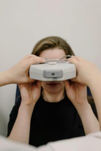 Unrecognizable female patient having eyesight check up with ophthalmic equipment while sitting on white background in professional clinic